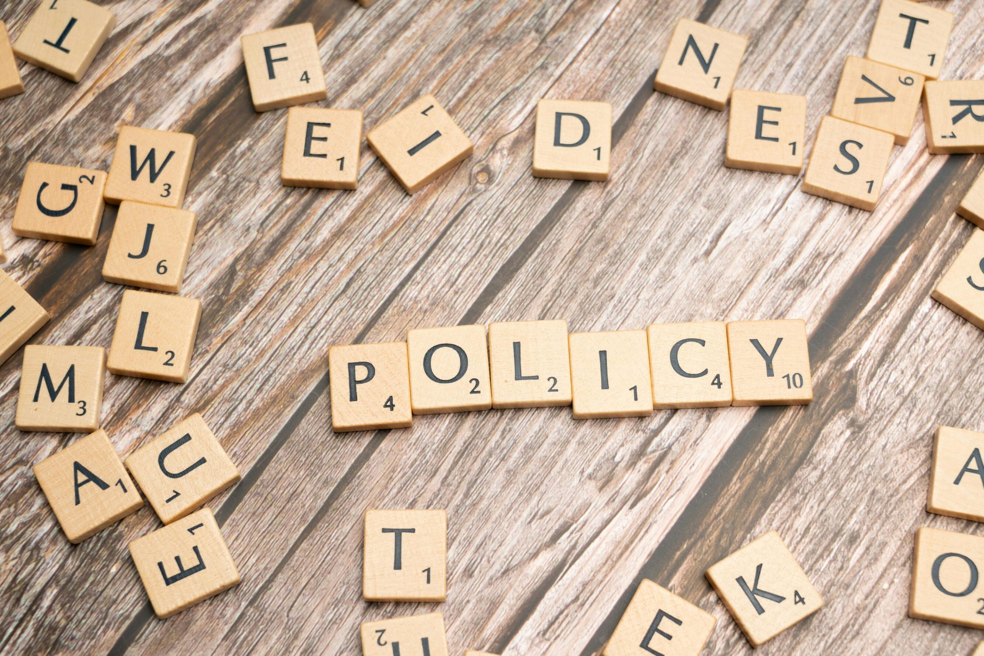 Scrabble tiles spelling "policy" on wood surface.