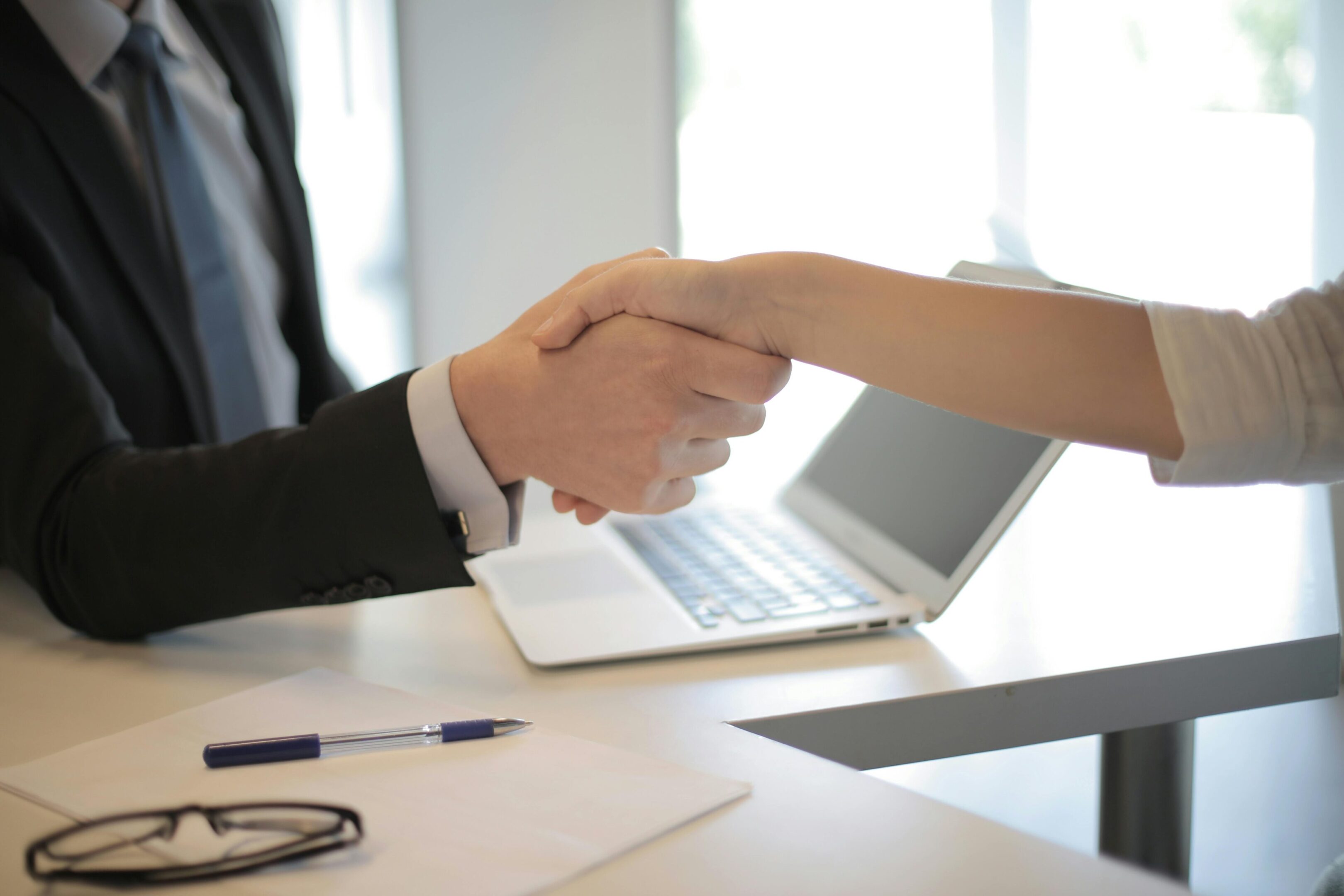 Handshake over a desk with laptop.