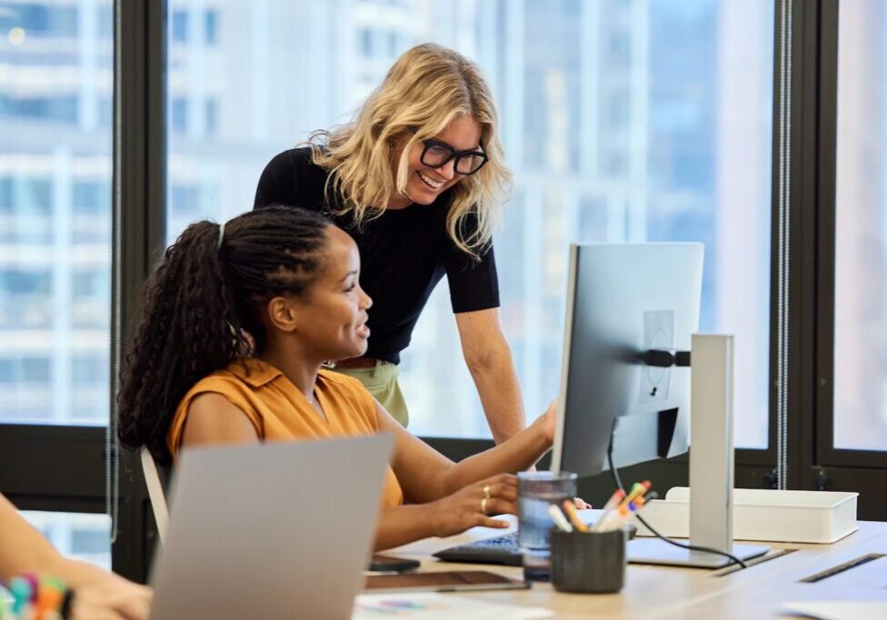 Women collaborating at a computer in office.