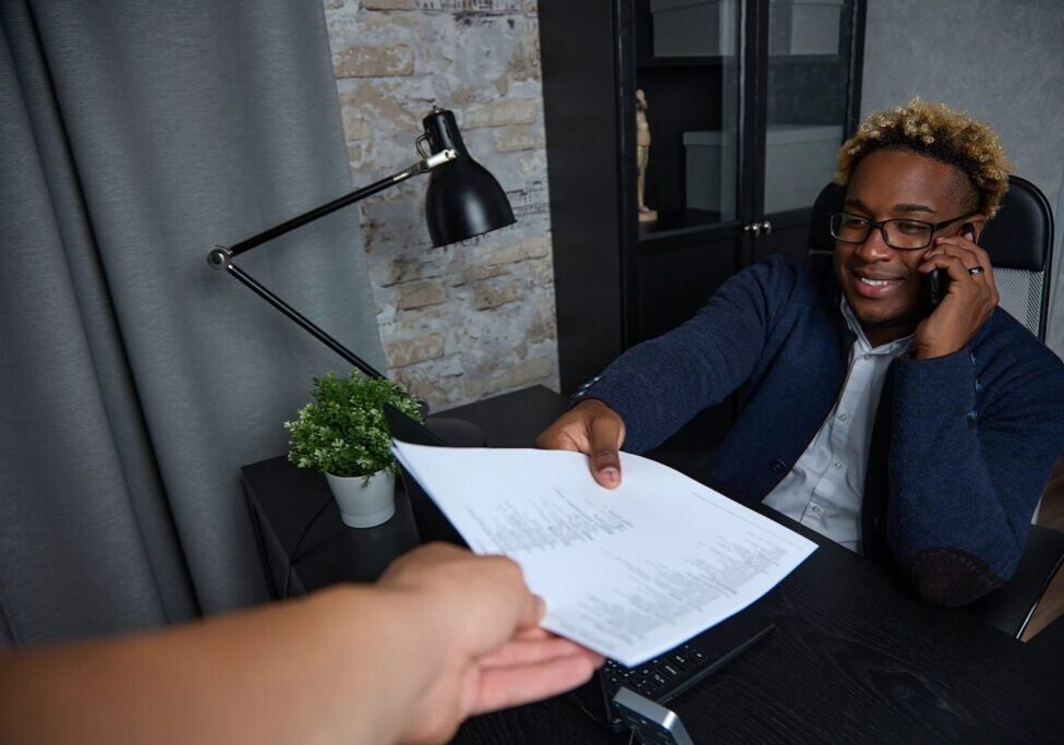 Man on phone receiving document at desk.