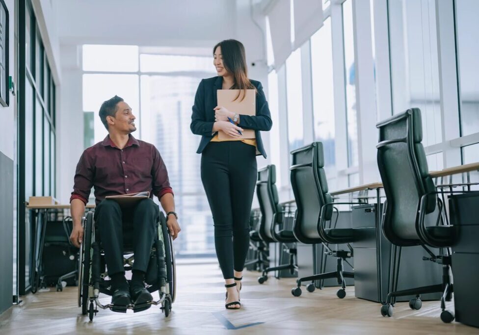 Man in wheelchair talking to colleague.
