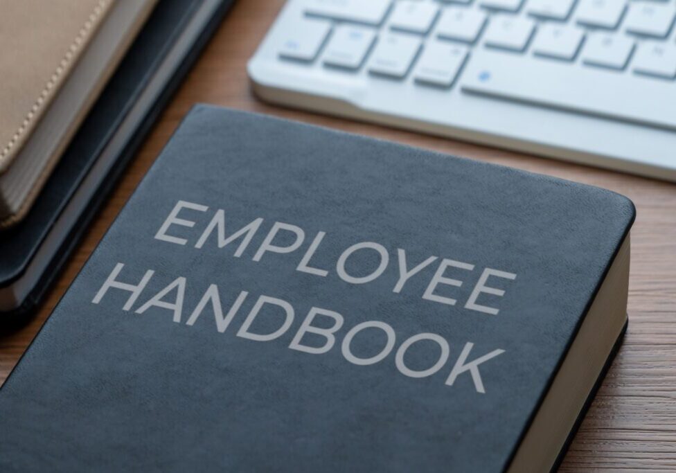 Employee handbook on a desk near keyboard.